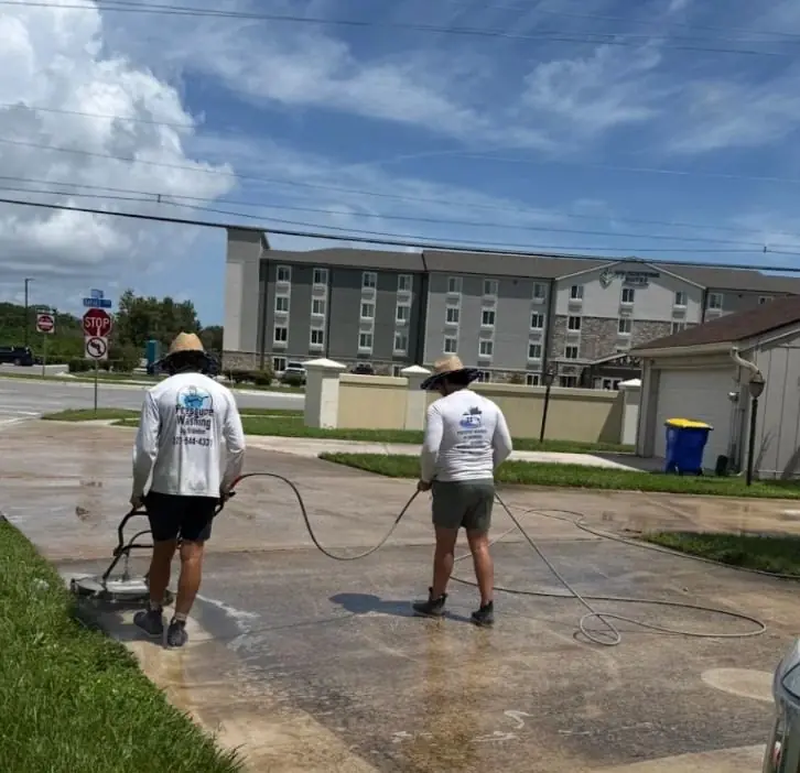 Two technicians pressure washing a commercial concrete entrance in Rockledge, FL