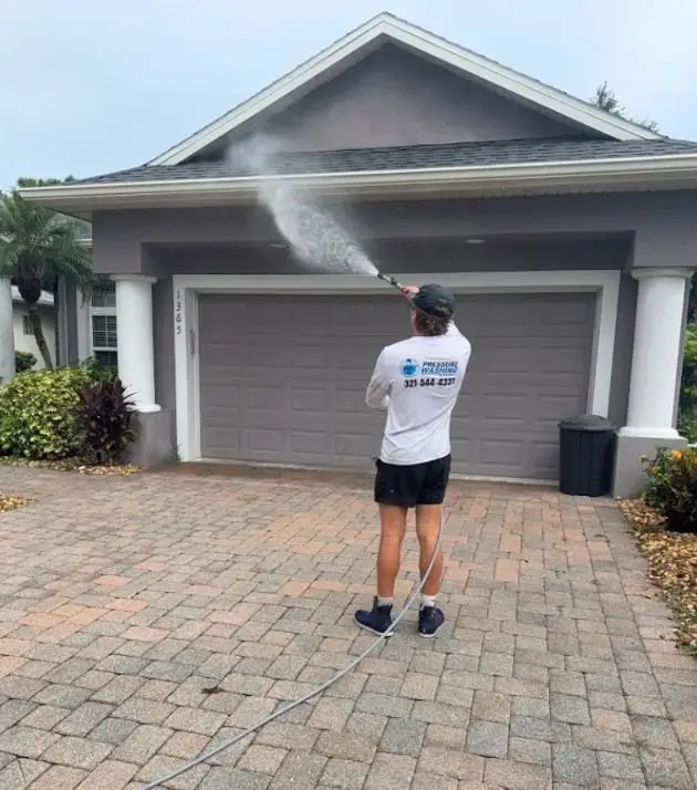 Technician soft washing the front of a home over a paver driveway in Melbourne, FL