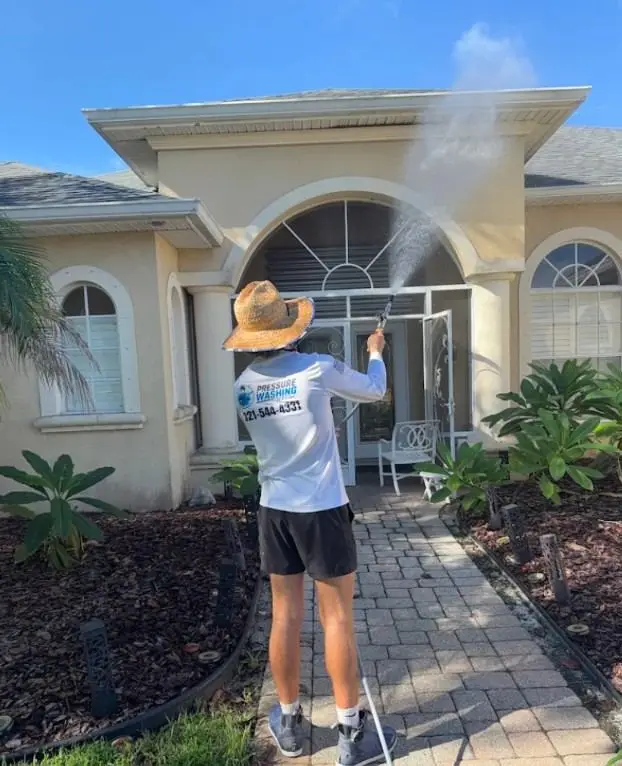 Technician soft washing a stucco home entry with arched windows in Rockledge, FL