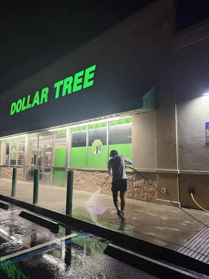 Technician pressure washing a retail storefront sidewalk at night in Rockledge, FL
