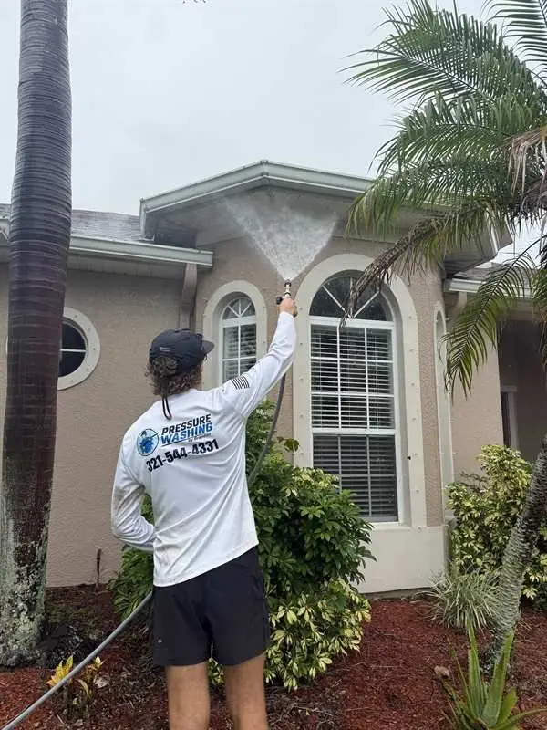 Technician soft washing stucco siding under a palm in Rockledge, FL