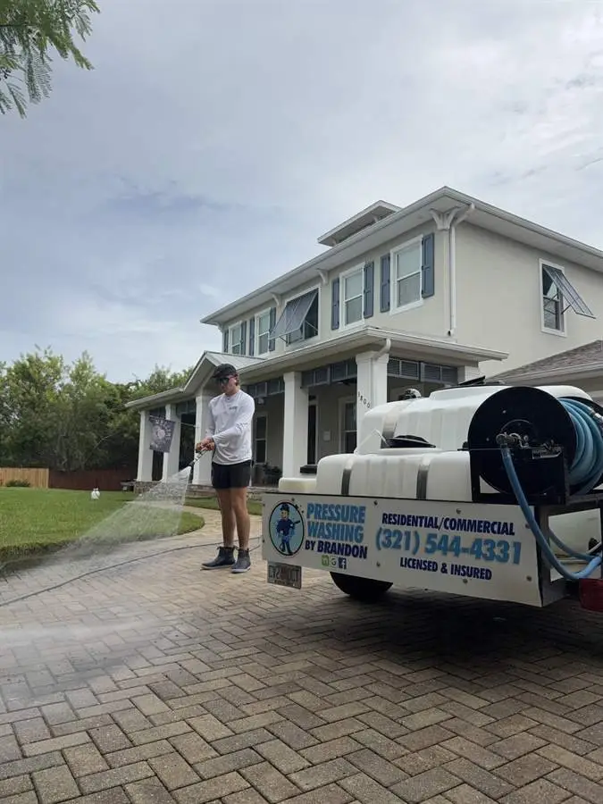 Technician rinsing a paver driveway beside the wash trailer at a Rockledge, FL home