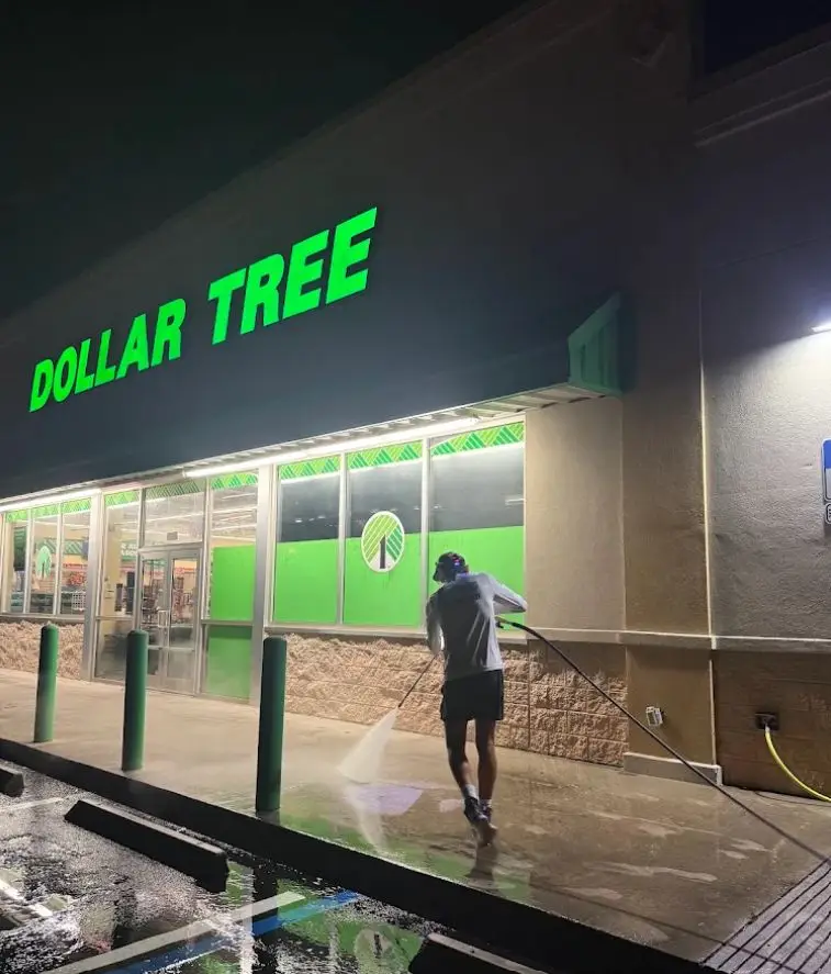 Technician pressure washing a retail storefront walkway at night in Rockledge, FL